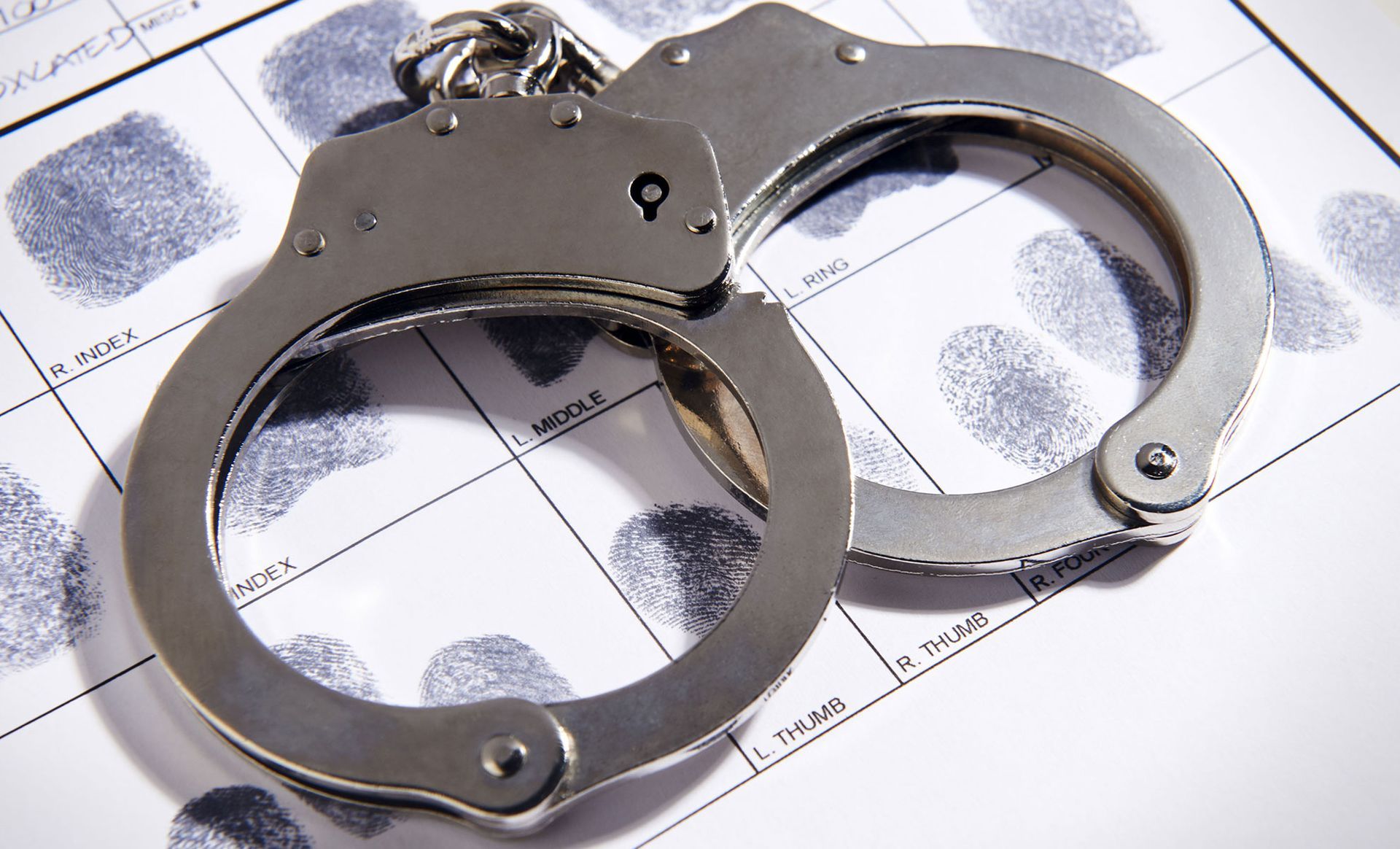 A pair of handcuffs laying on top of a sheet of fingerprints