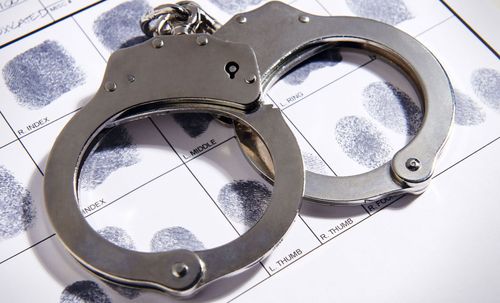 A pair of handcuffs laying on top of a sheet of fingerprints