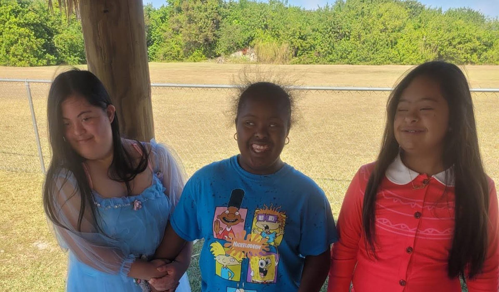 Three people standing under a wooden shelter outdoors, posing and smiling at the camera.