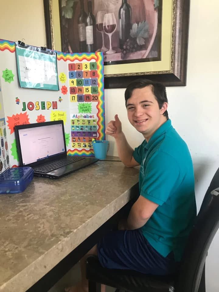 Person smiling at a desk with a laptop and colorful educational posters on the wall