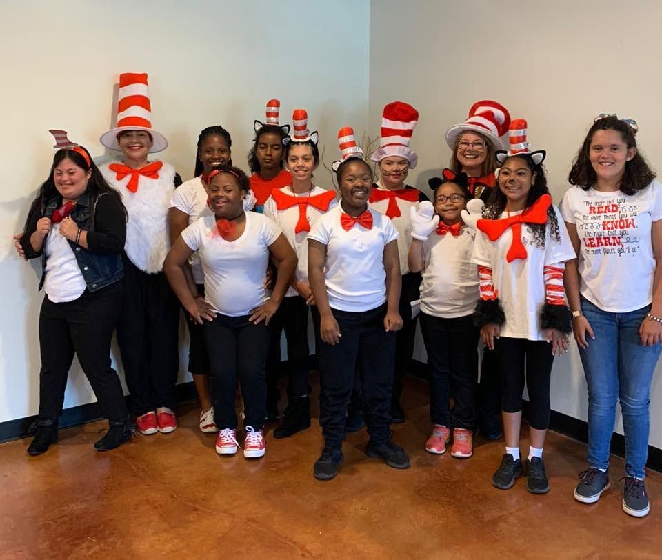 Group of people in red-and-white Dr. Seuss-style hats posing indoors, smiling at the camera.