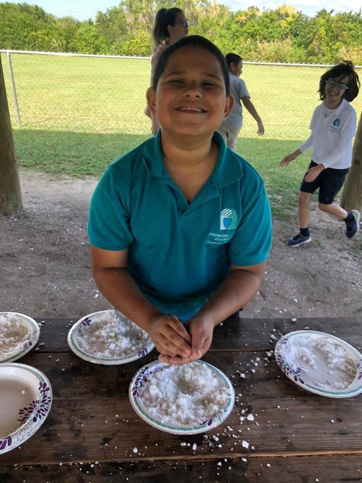 Smiling child in teal shirt at picnic table with pies, outdoors under a shelter