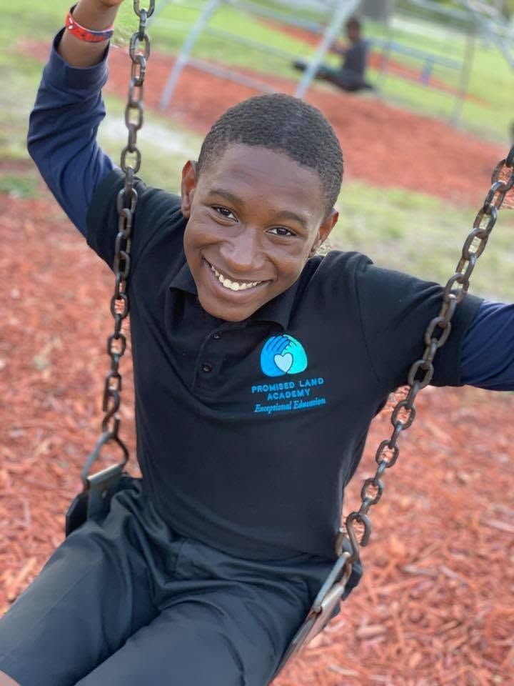 Smiling person on a swing at a playground, wearing a black shirt with a blue logo.