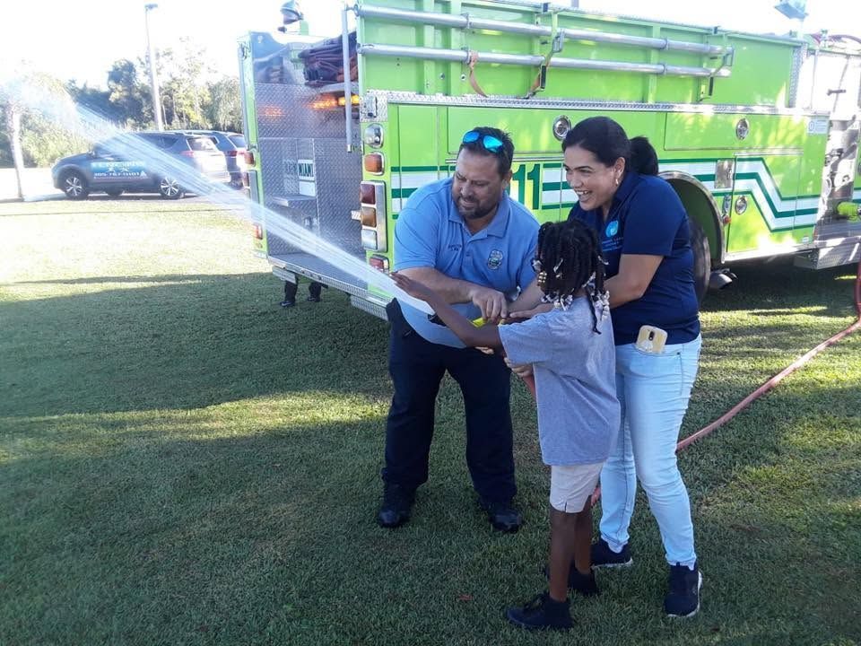 Three people holding a large sheet beside a bright green truck on a grassy lawn.
