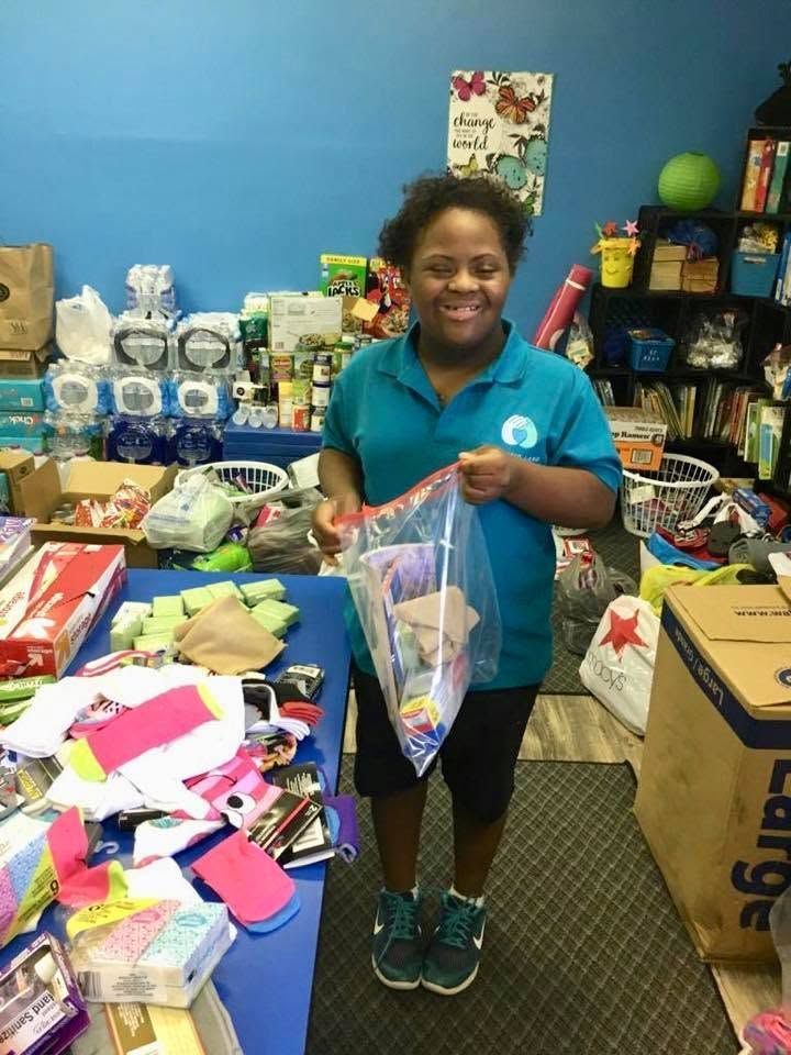 Person smiling in a room full of supplies, holding a clear gift bag with colorful items.