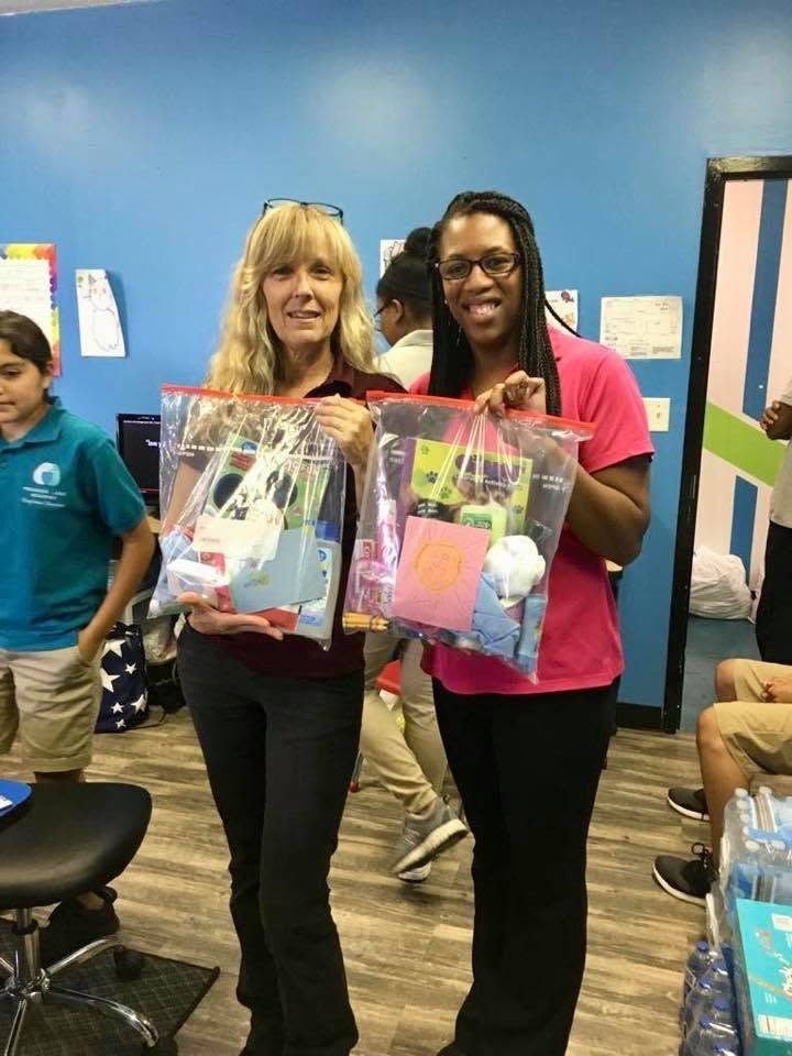 Two people holding gift bags in a classroom, standing in front of a blue wall.