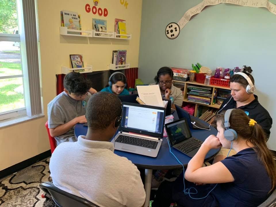 Students gathered around laptops in a classroom, working together at a round table.
