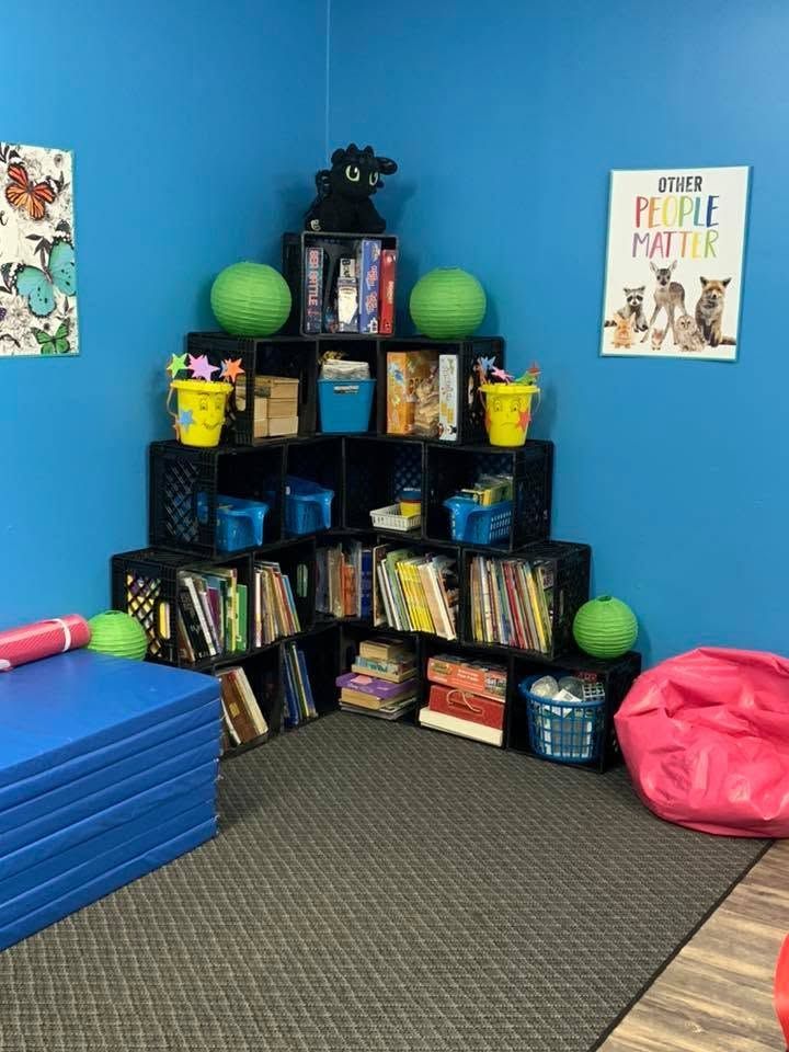 Children's reading nook with a black bookshelf, colorful books, bean bags, and blue wall decor