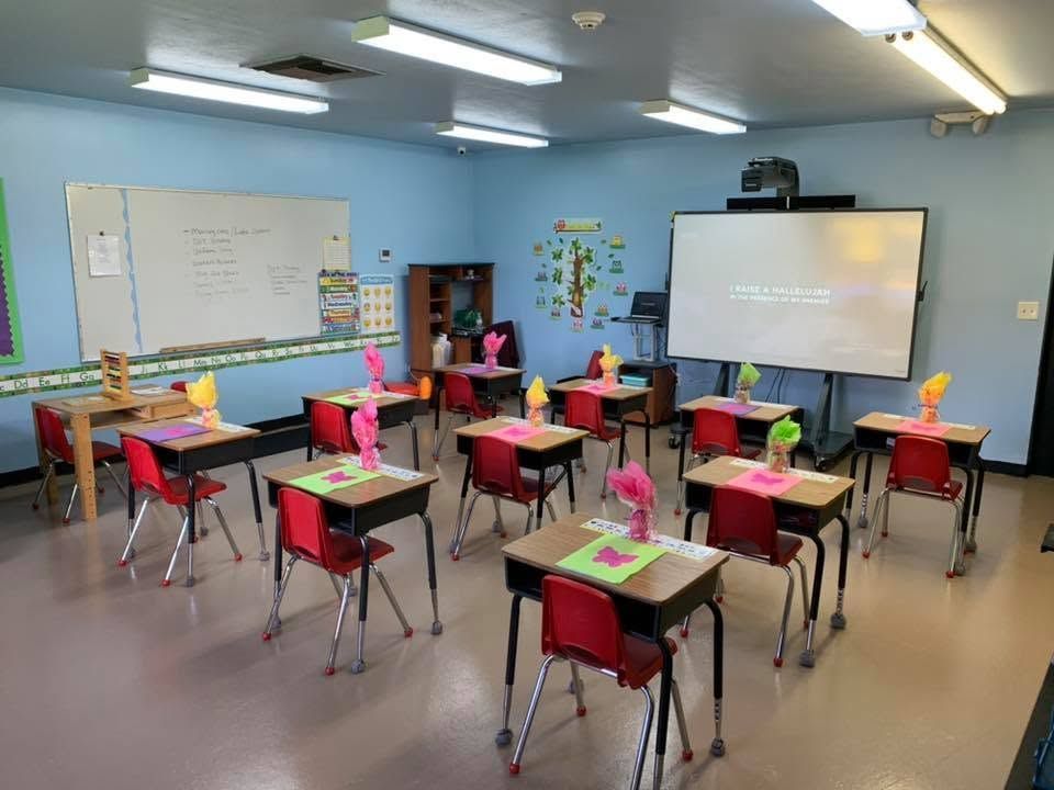 Empty classroom with colorful desks, whiteboard, and projector screen in a bright, blue-walled room