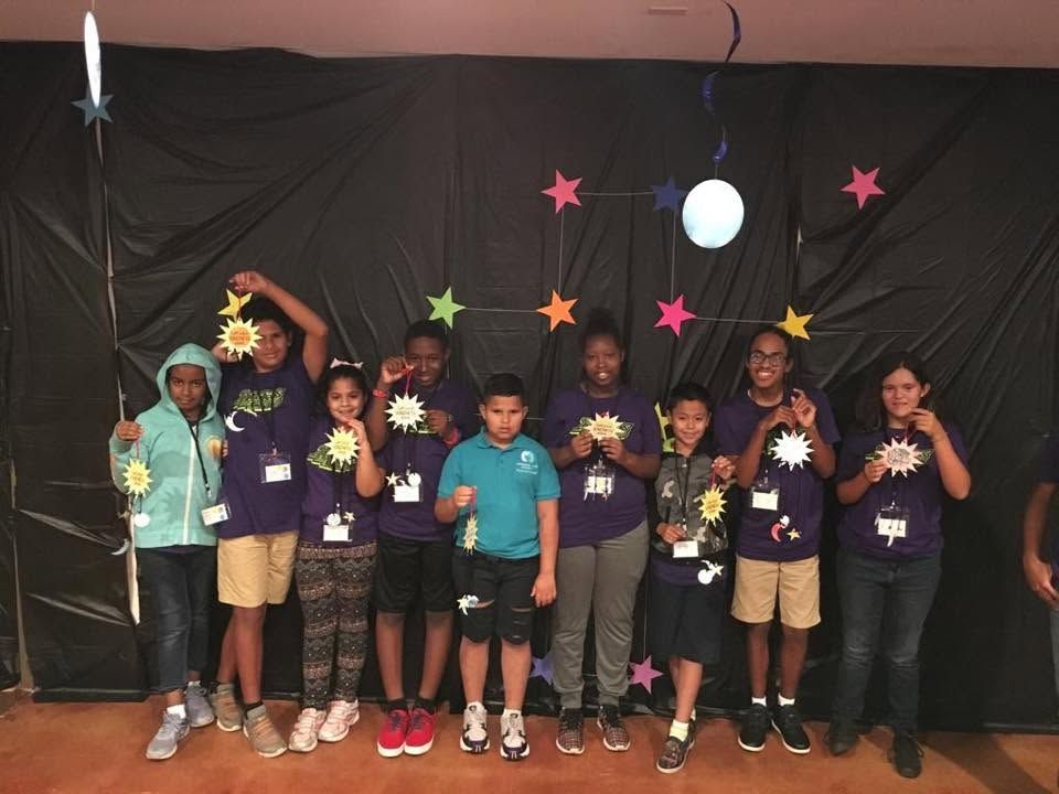 Group of children posing on stage with star decorations and a moon backdrop, holding awards and smiling.