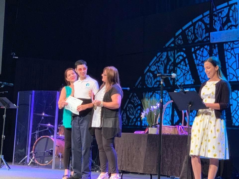 Four people stand onstage with an award certificate and bouquet during a ceremony.