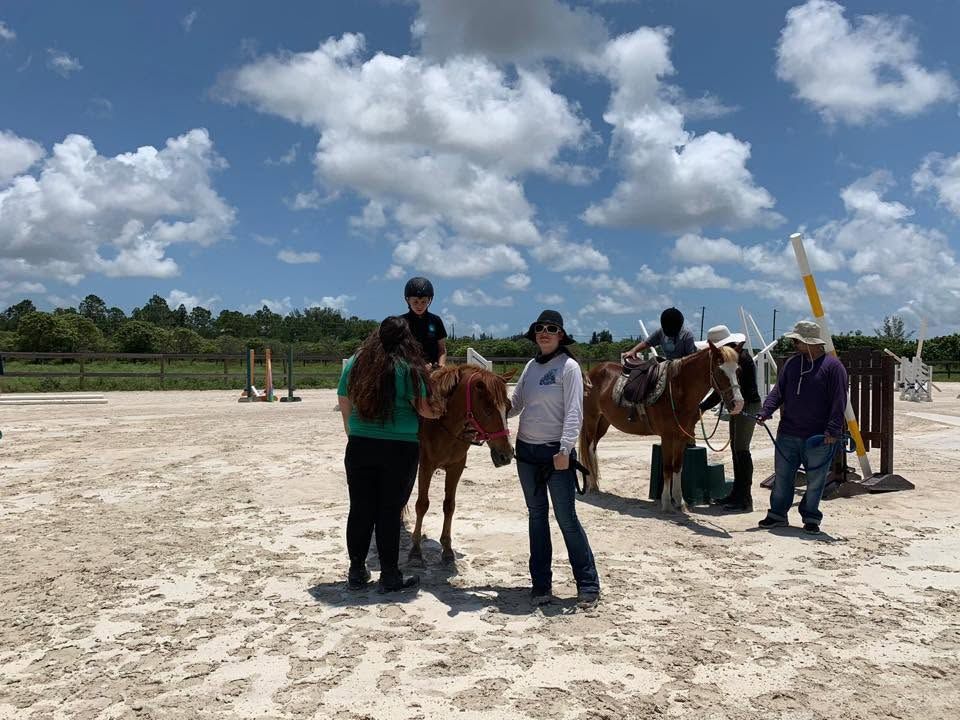 People standing with horses on a sandy trail under a bright blue sky with scattered clouds