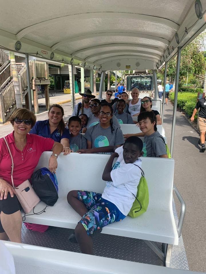 Group of people riding together on an open tram, smiling under a covered roof at a park.