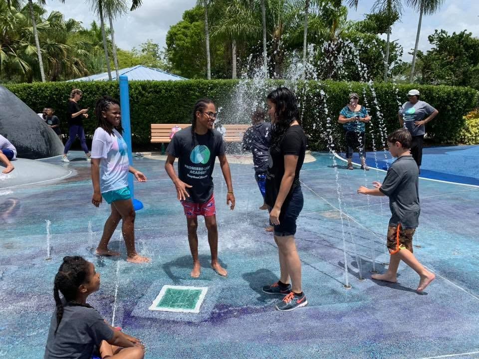 Children playing in a colorful outdoor splash pad with water jets on a sunny day