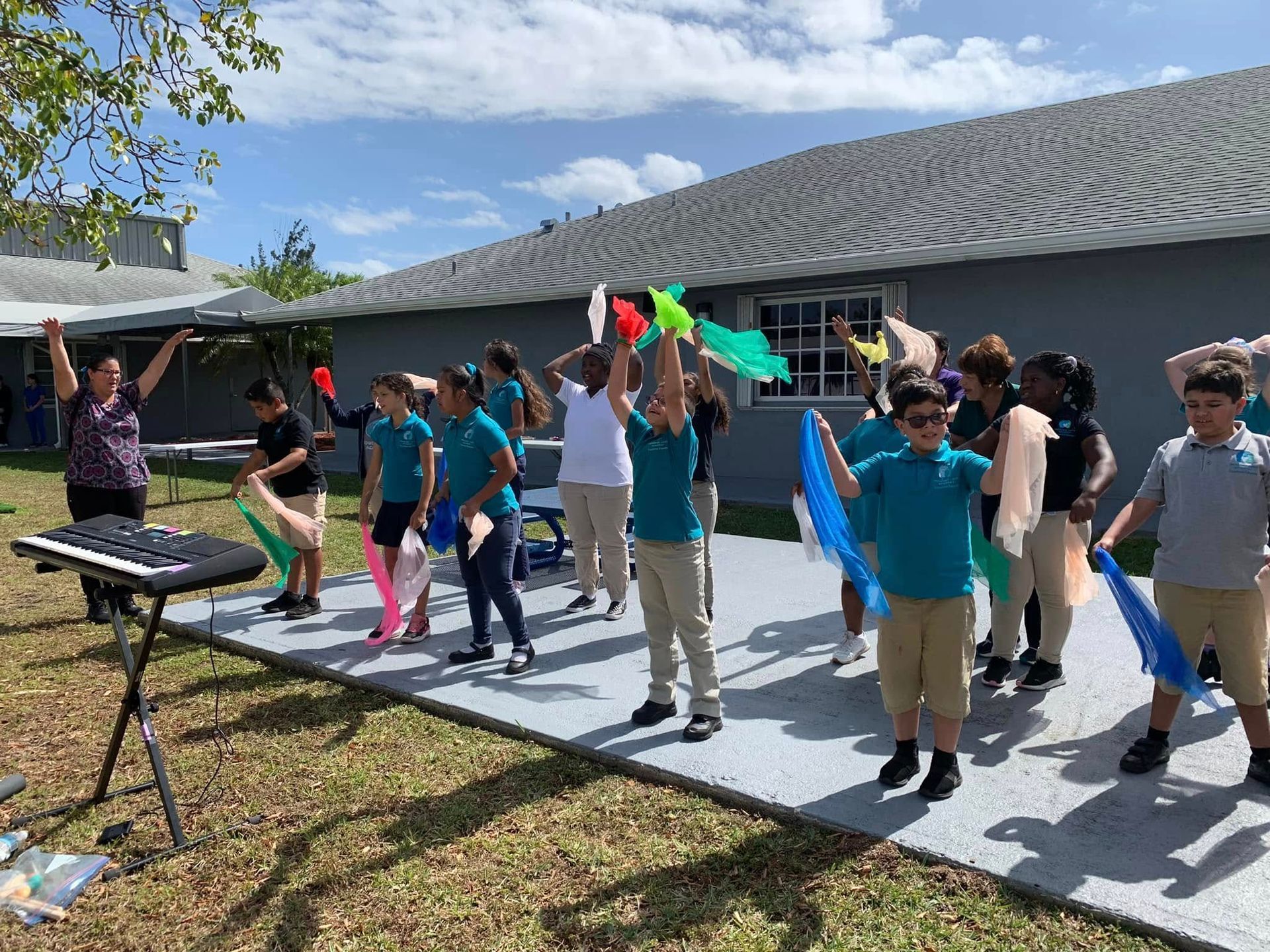 People exercising outdoors on a sunny patio, holding colorful foam noodles near a house.