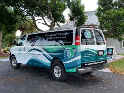 White and teal company van parked outdoors under trees with branding and a phone number on the side