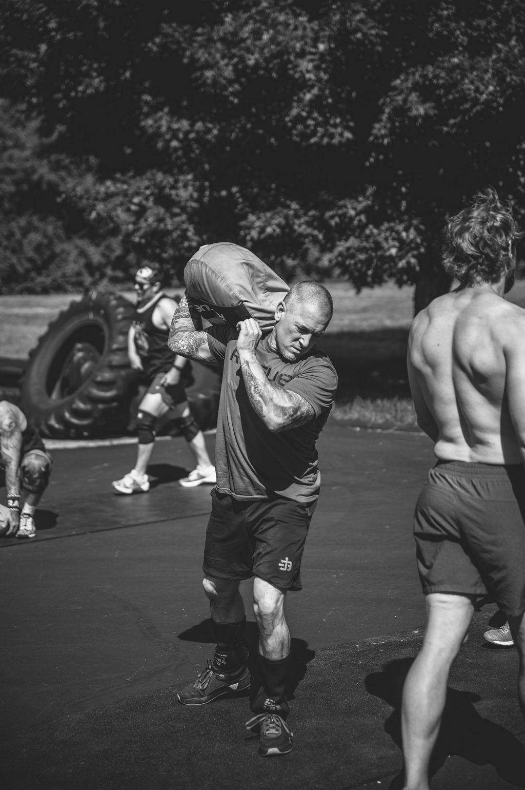 Black-and-white photo of athletes training outdoors, with one man carrying another on his shoulders.