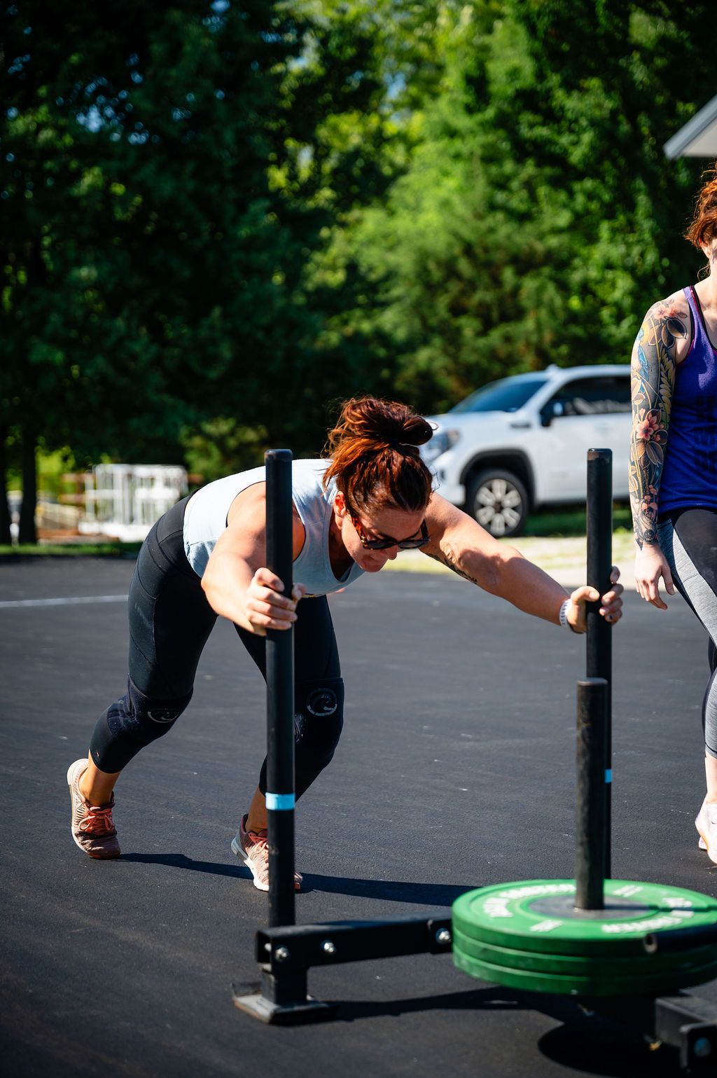 Person pushes a weighted sled on an outdoor track beside a green plate weight.