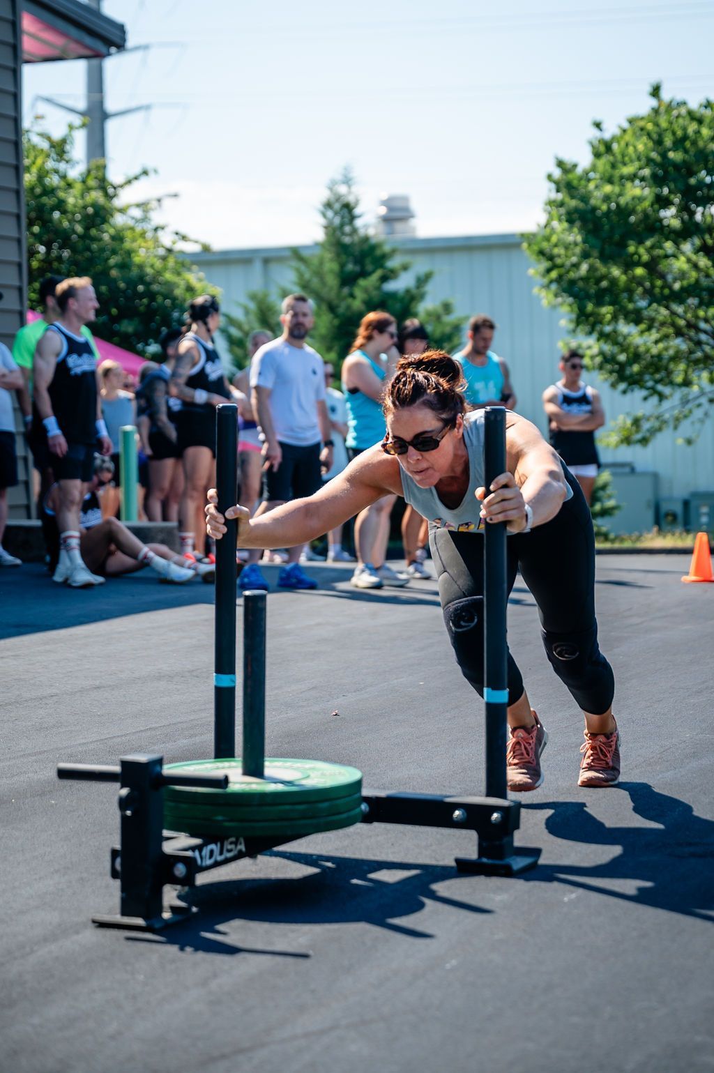 Person pushing a weighted sled on an outdoor course, with spectators in the background