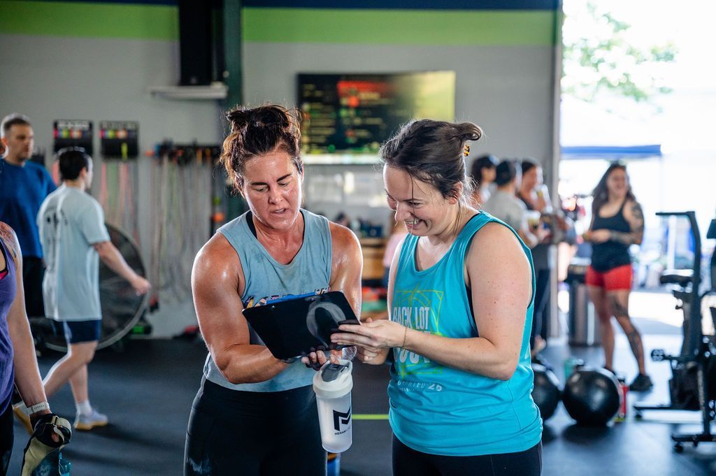 Two people in a gym reviewing a fitness device, with exercise equipment in the background