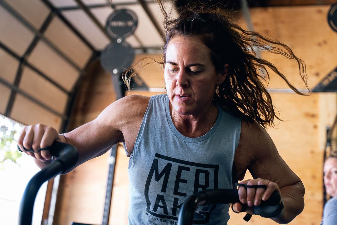 Woman exercising on a stationary bike in a gym, wearing a gray tank top and focused expression