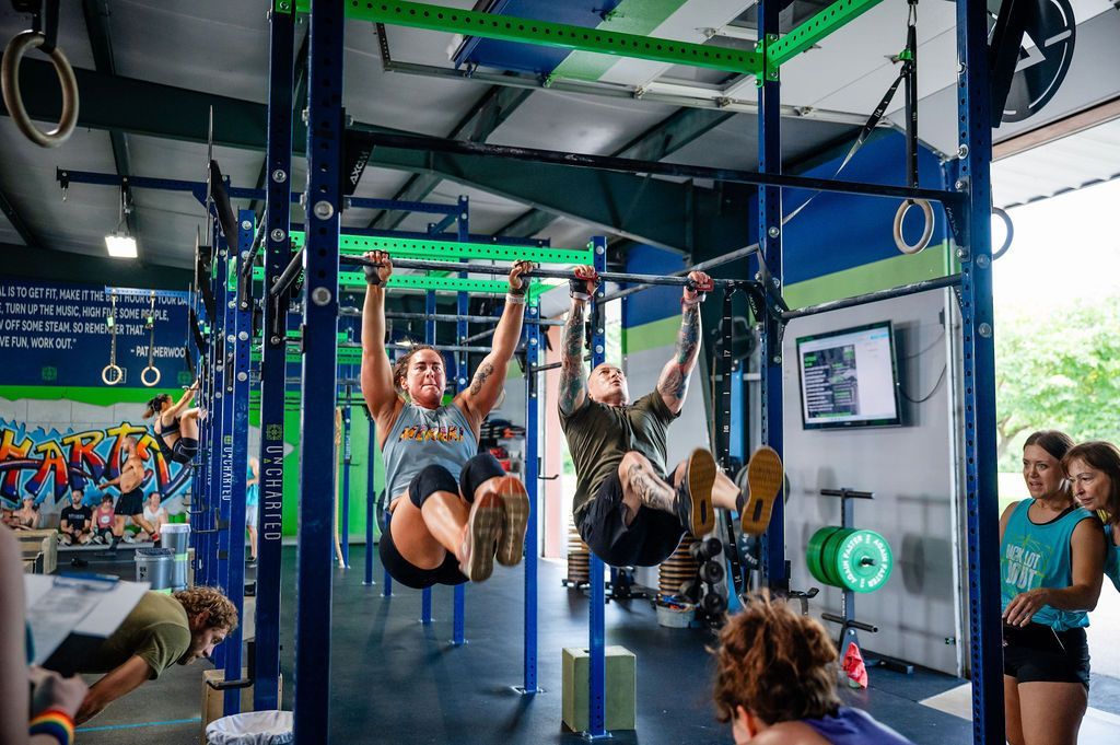 People doing hanging leg raises in a gym fitness class with blue and green rigging