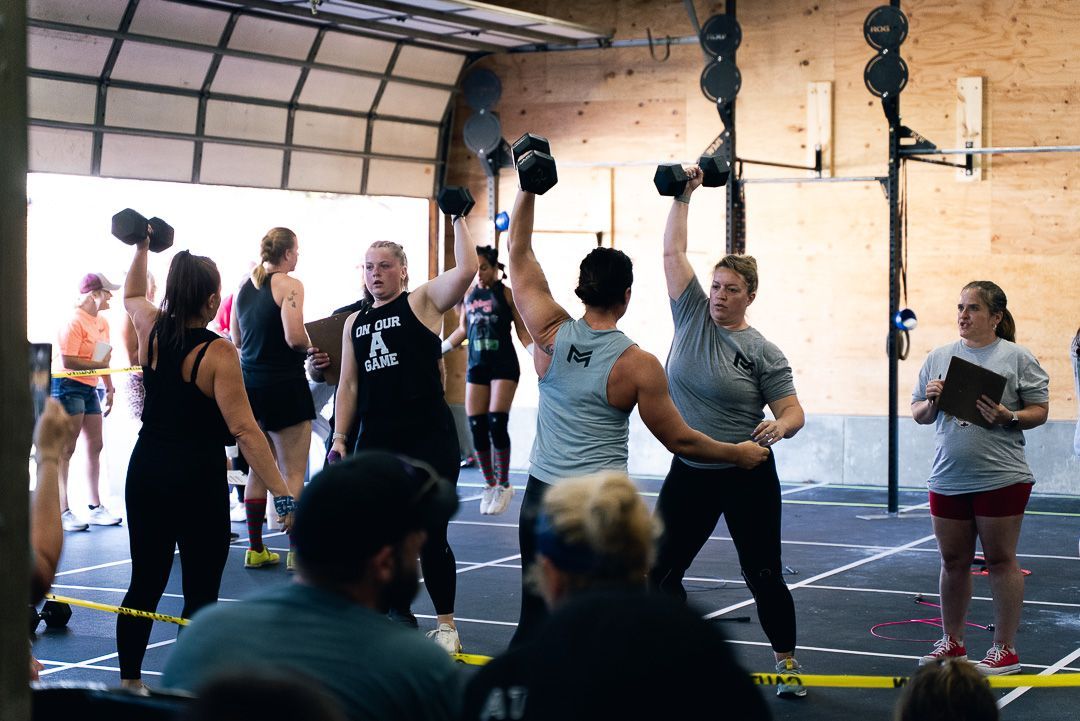 People exercising in a gym, lifting kettlebells overhead in a group workout class.