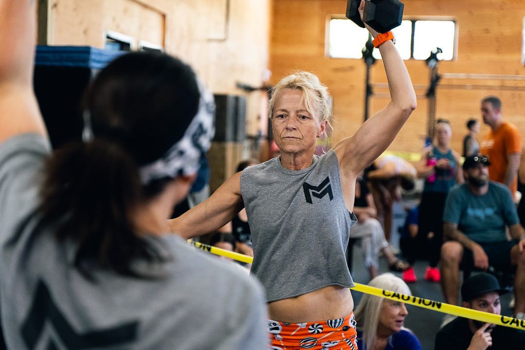 Female athlete lifting a black kettlebell in a gym competition, with spectators and caution tape behind her