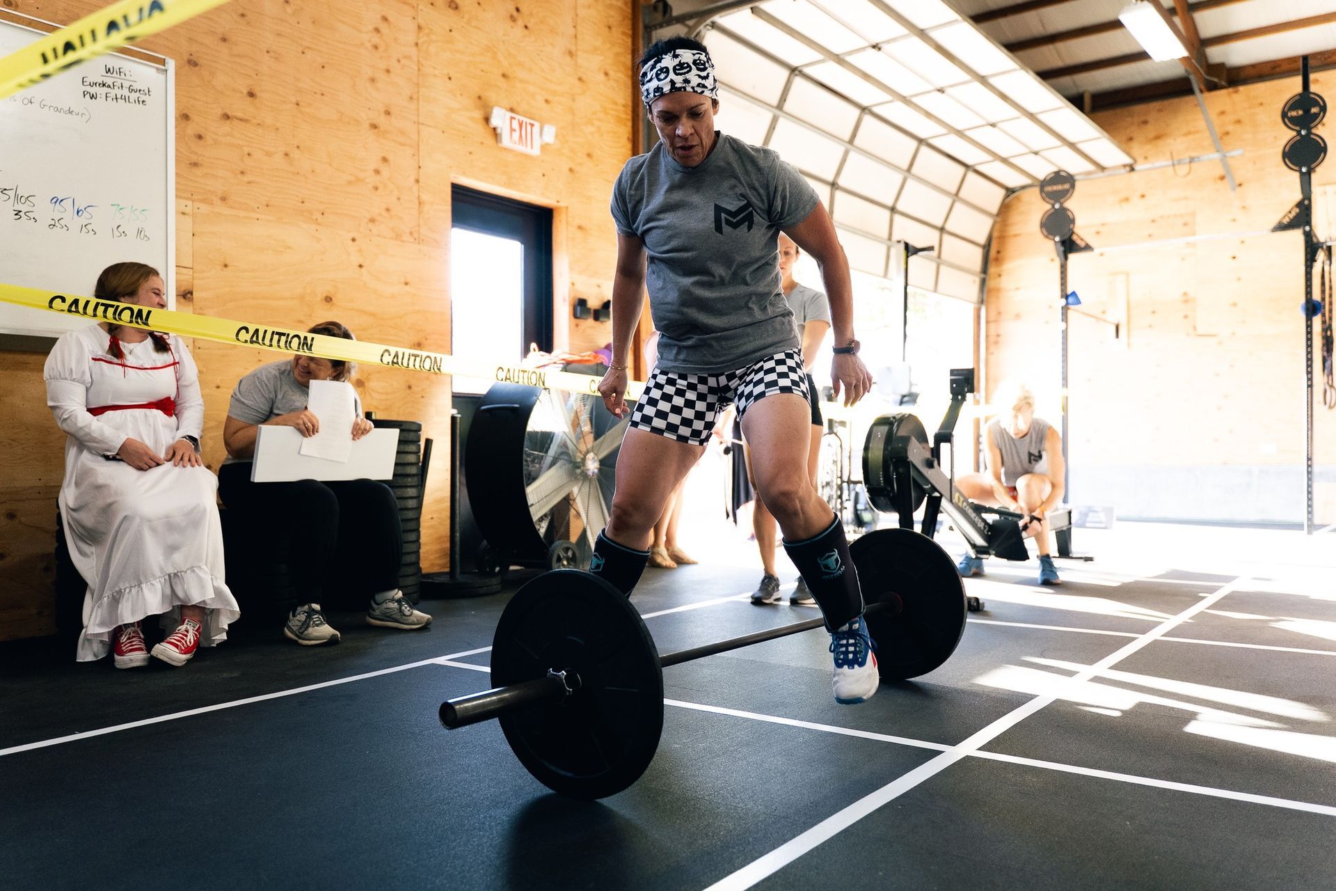 Athlete deadlifting in a gym, with spectators seated in the background.