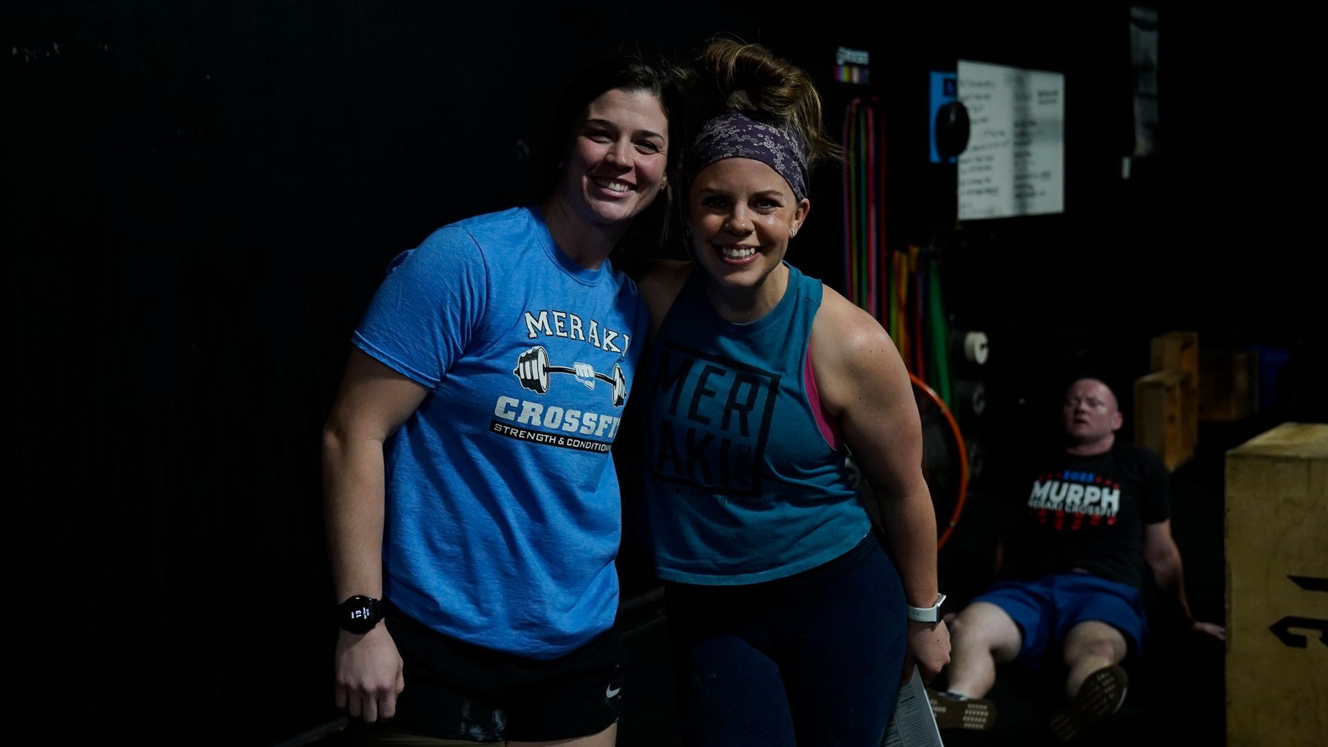 Two athletes smiling in a gym, standing close together in blue workout shirts and black shorts