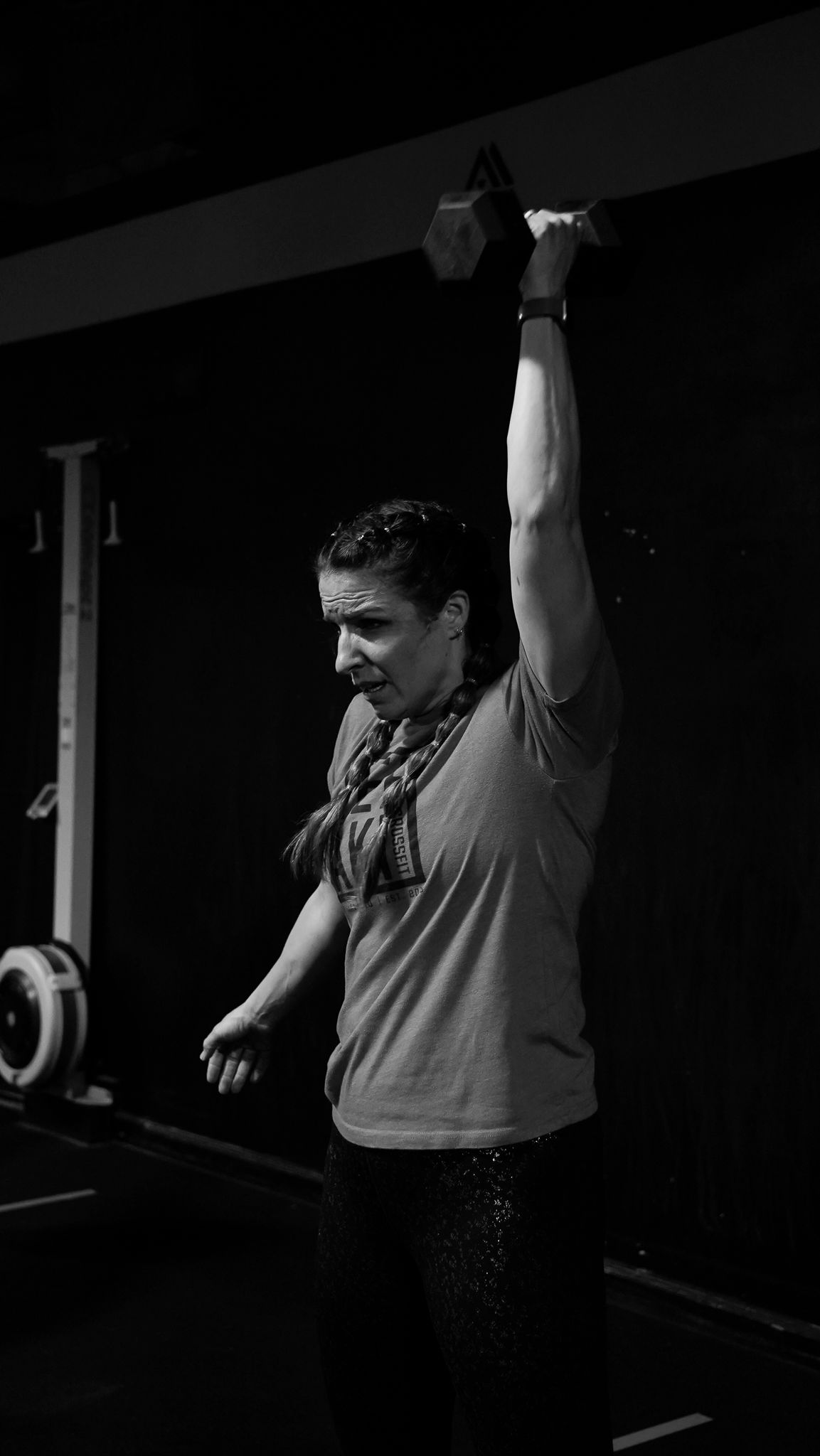 Woman lifting a dumbbell overhead in a gym, focused during a workout.