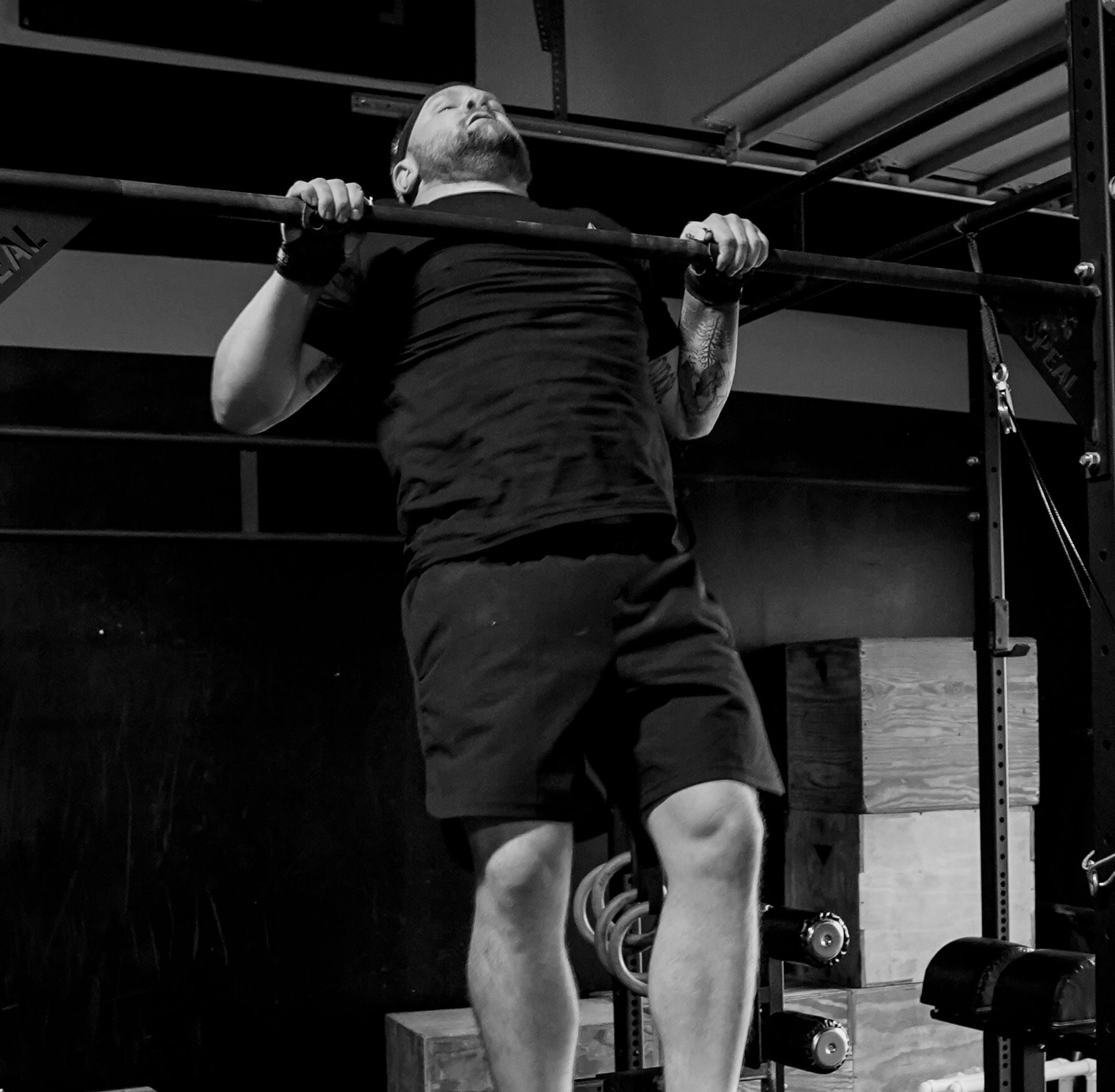 Person doing a pull-up on a gym bar, viewed from below in black and white.