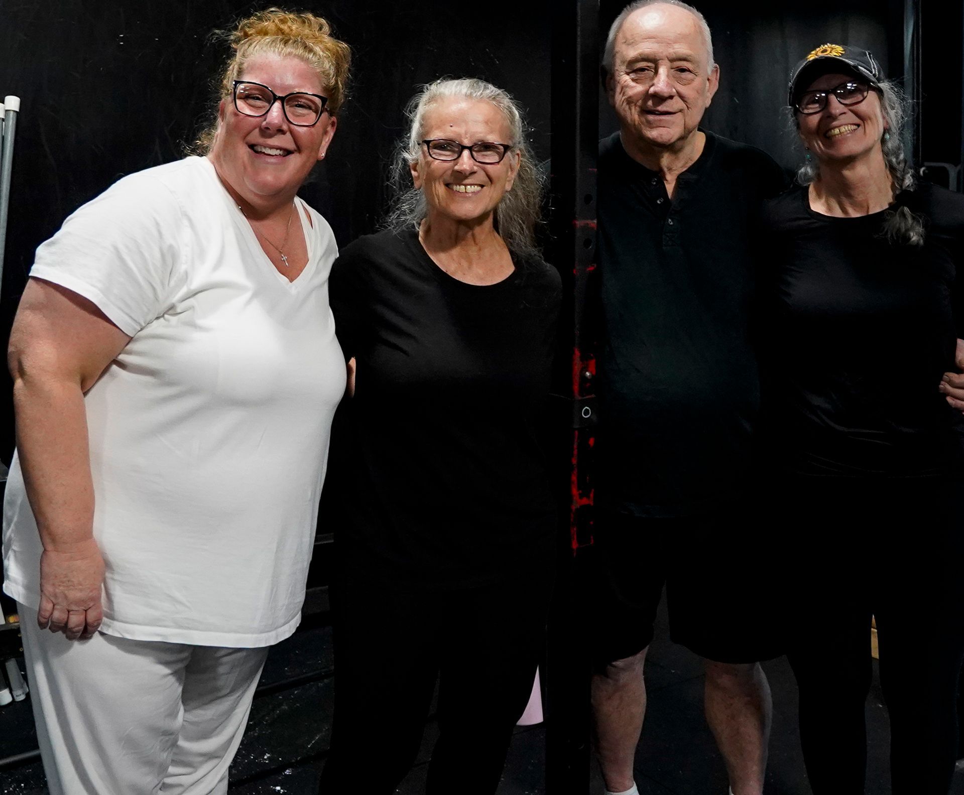 Four adults posing together indoors, smiling in mostly black and white clothing.