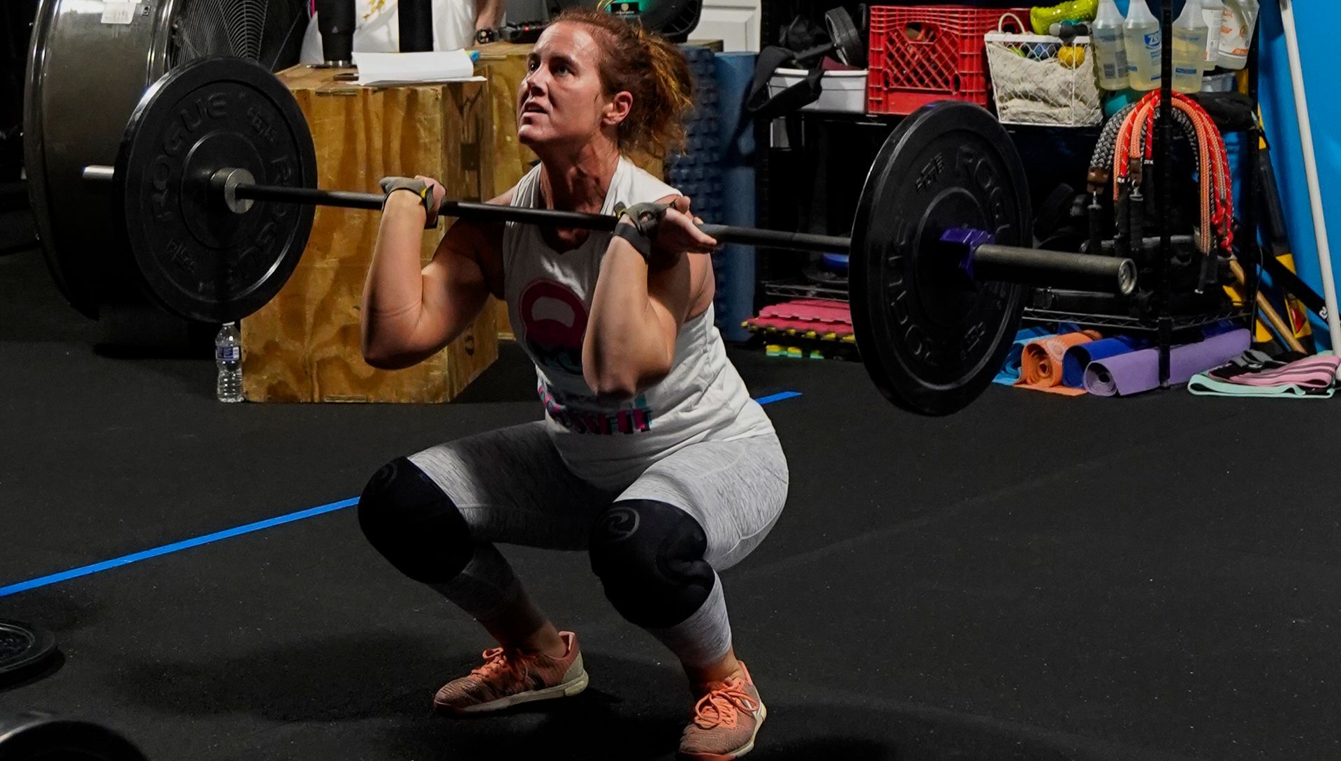 Woman performing a front squat with a barbell in a gym, focused and crouched low.