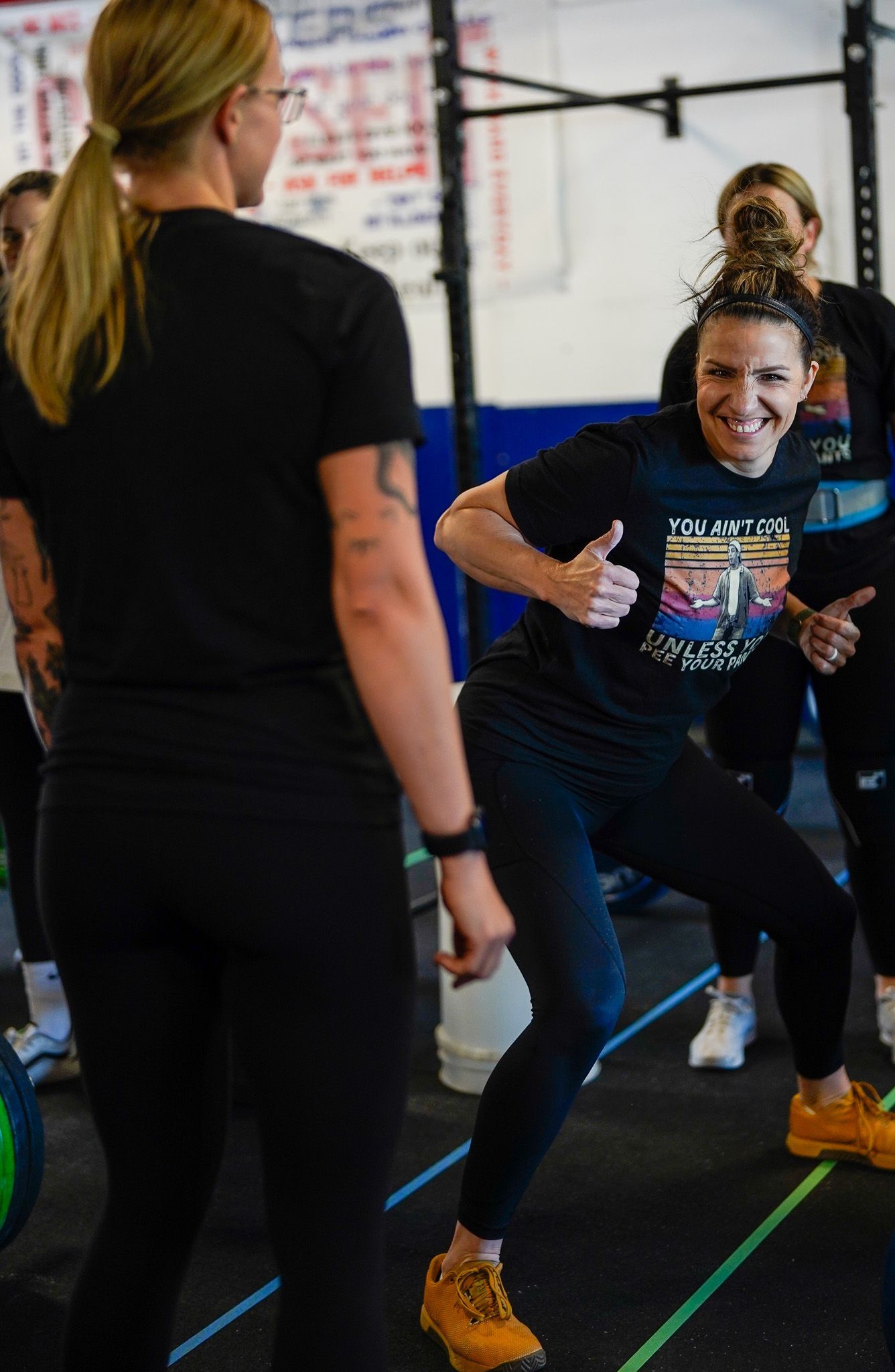 Woman in a gym doing a squat while smiling, with a trainer standing nearby.