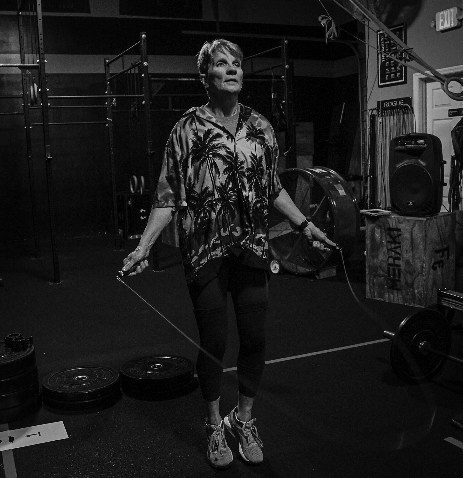 Woman skipping rope in a gym, wearing a patterned shirt and leggings, with weights and equipment nearby