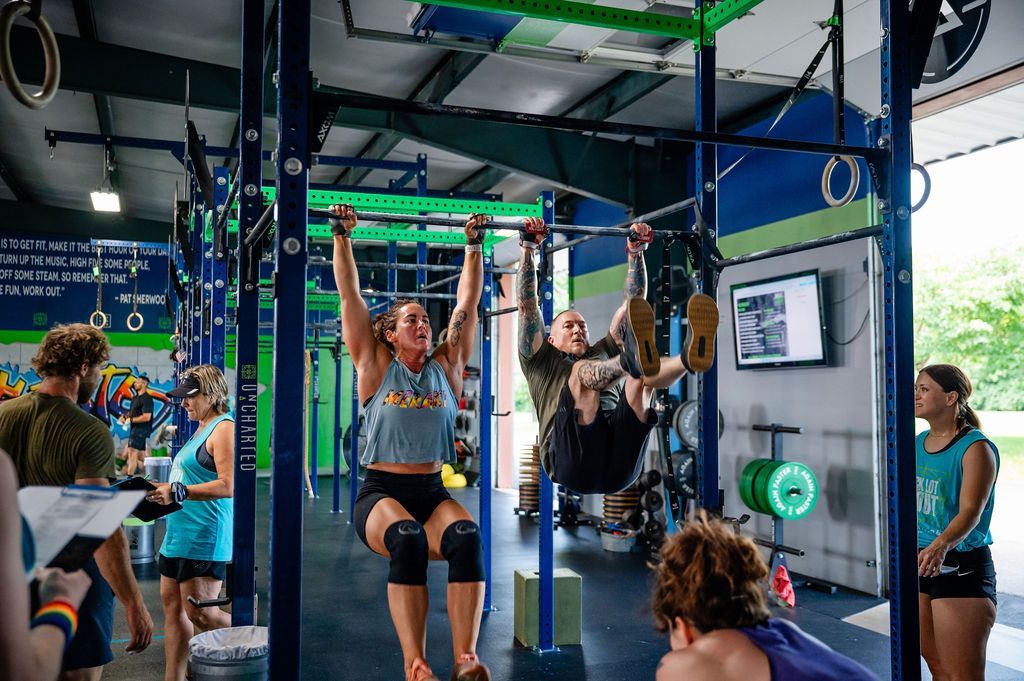 People doing pull-ups in a gym fitness class with colorful equipment and monitors