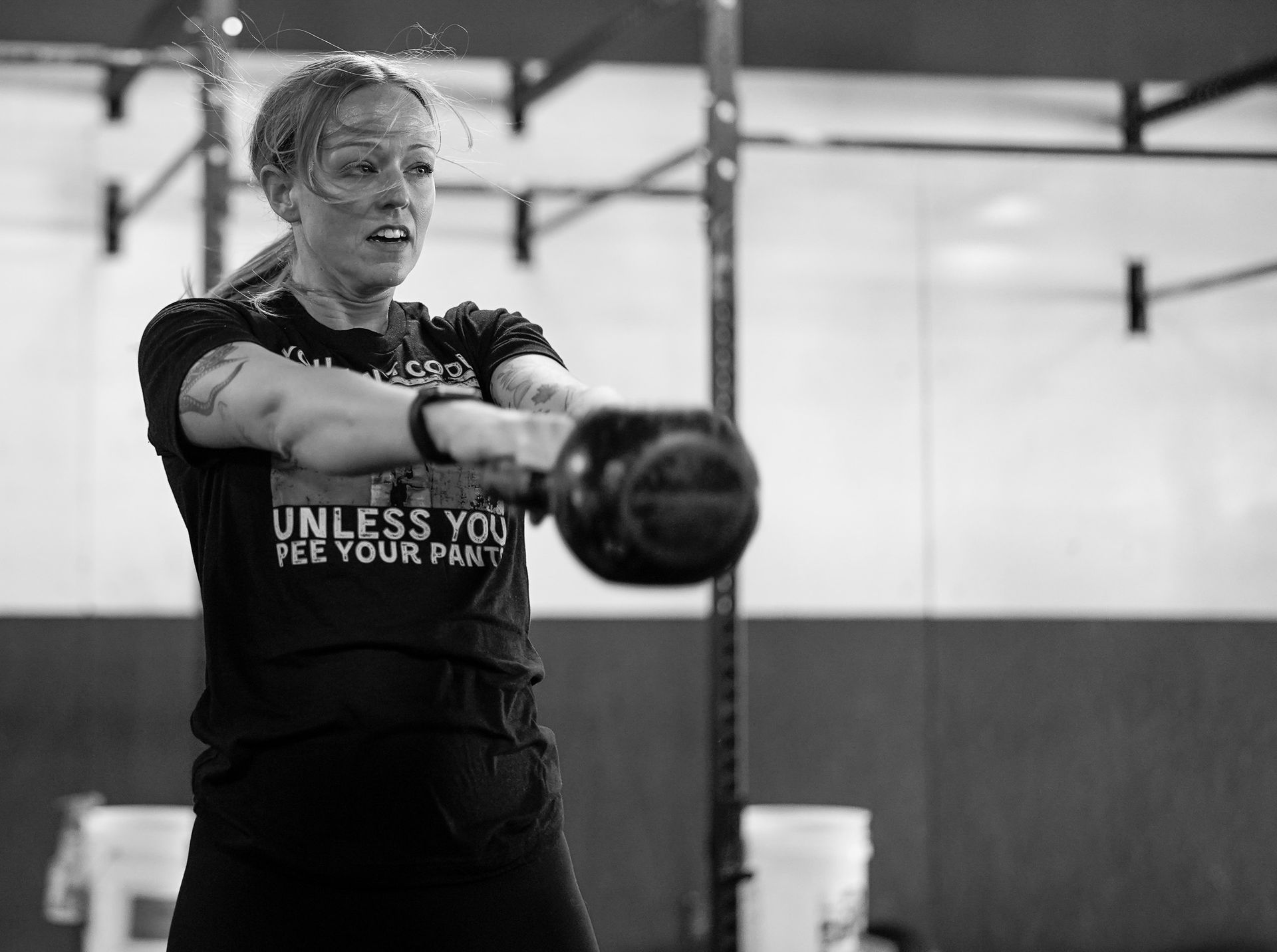 Person exercising with a kettlebell in a gym, holding it out in front with focused expression.
