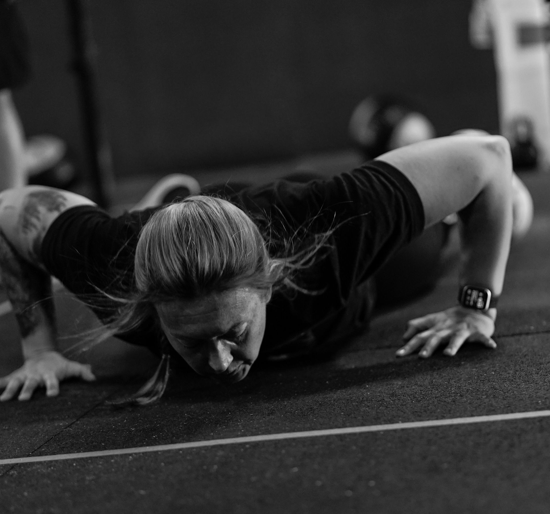 Black-and-white close-up of a person doing a push-up on a gym floor, face focused.