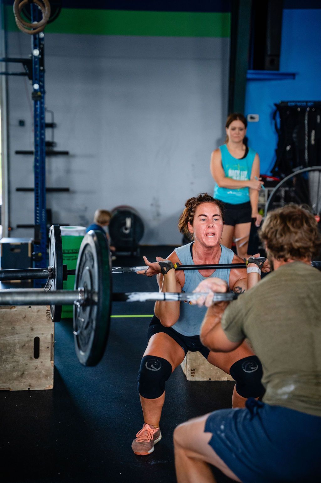 Woman lifting a barbell in a gym as a coach spots her from the front