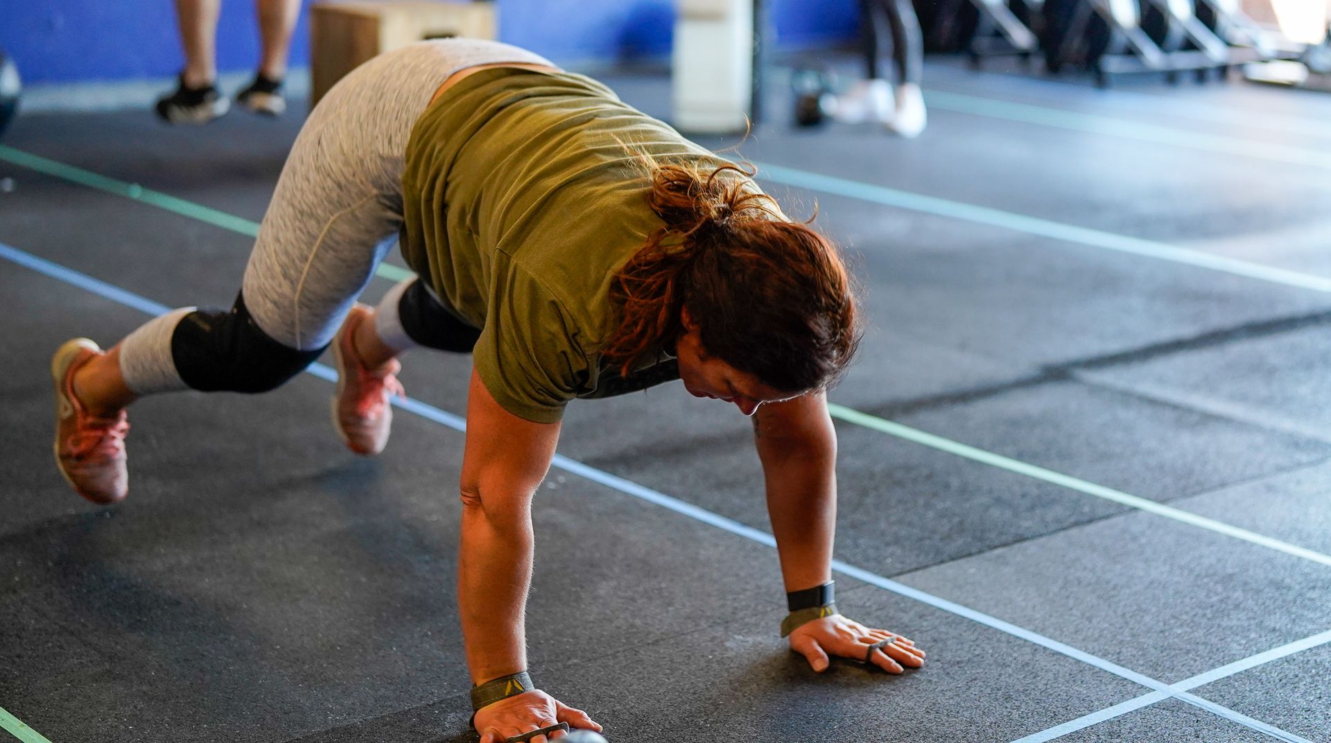 Person in a plank position during a workout on a gym floor, wearing a green shirt and black leggings.