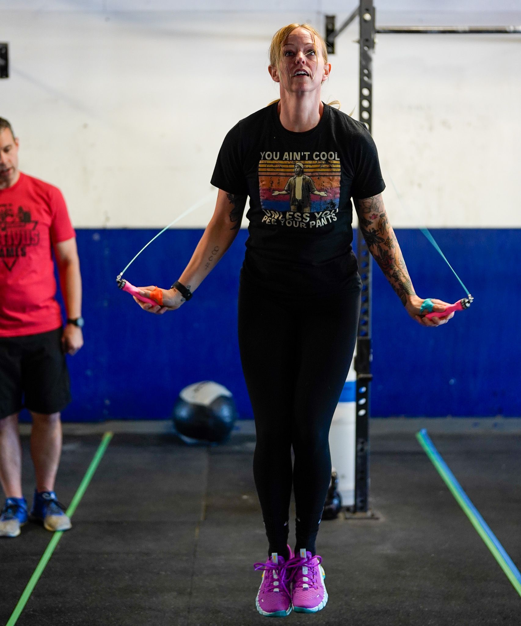Person skipping rope in a gym, wearing black leggings and a black shirt, with a blue wall behind.
