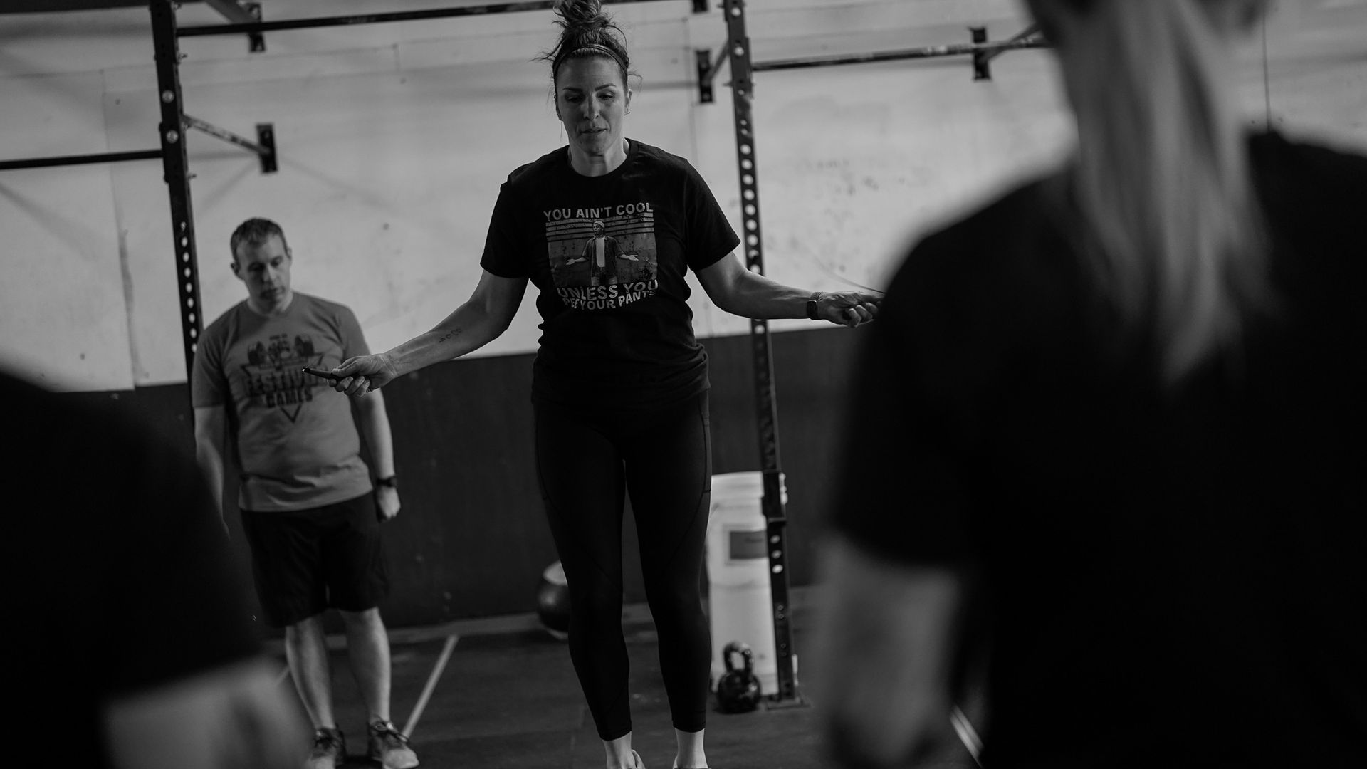 People exercising in a gym, with one woman jumping rope in the center.
