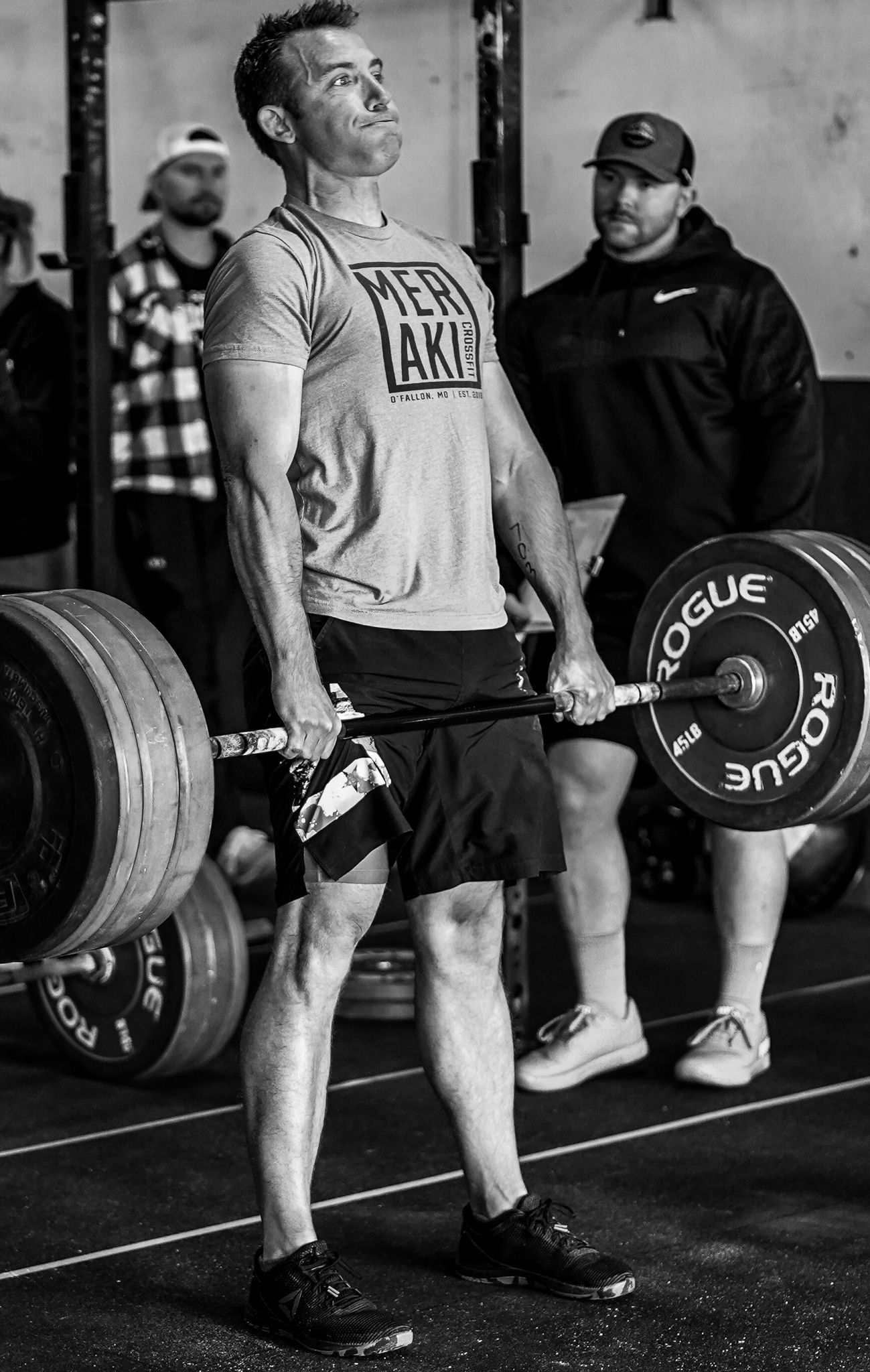 Powerlifter deadlifts a loaded barbell in a gym while a coach watches nearby.