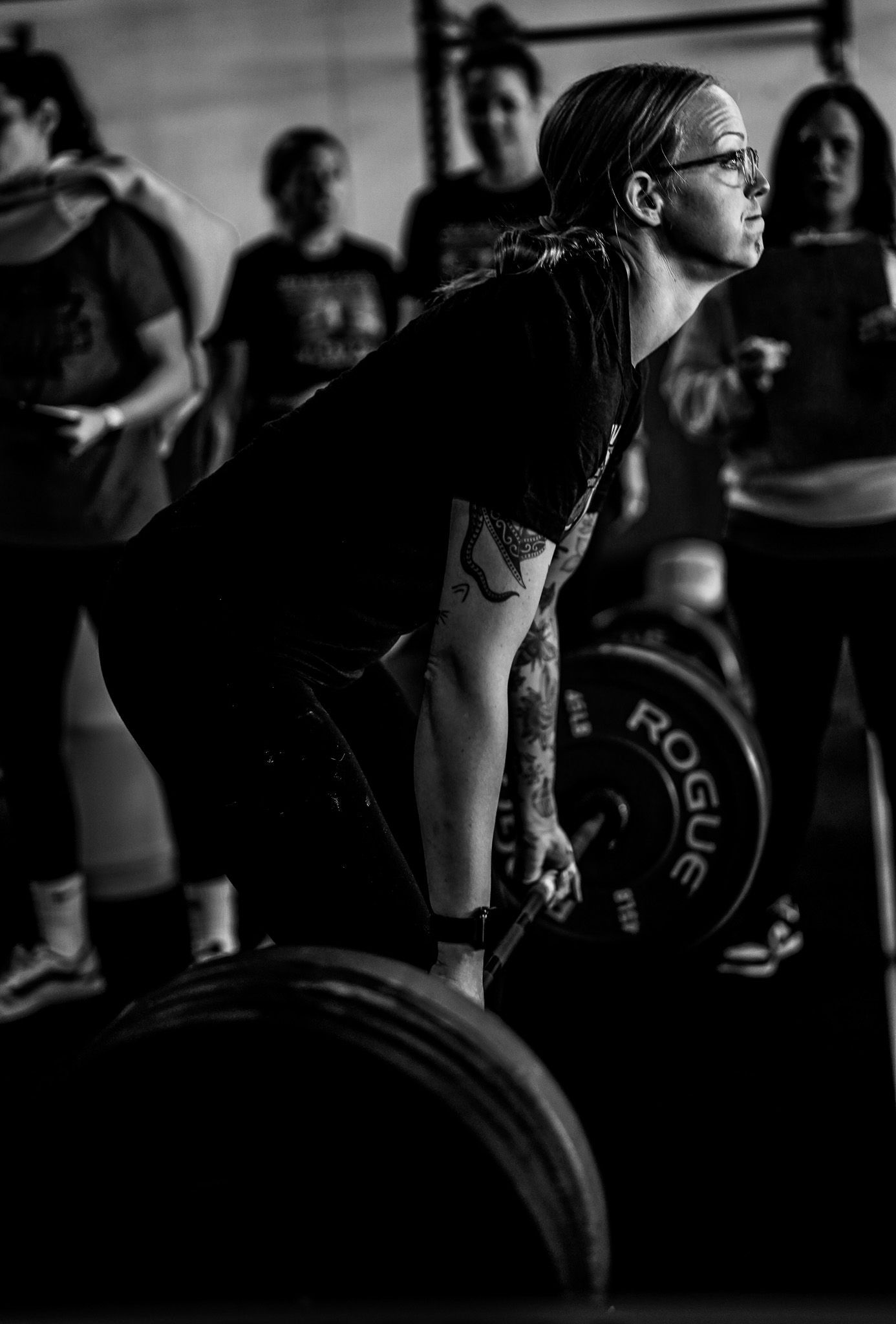 Person deadlifting a barbell in a gym, with others blurred in the background.