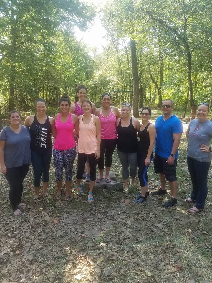 Group of eight people standing on a forest trail in athletic clothes, smiling for a group photo.