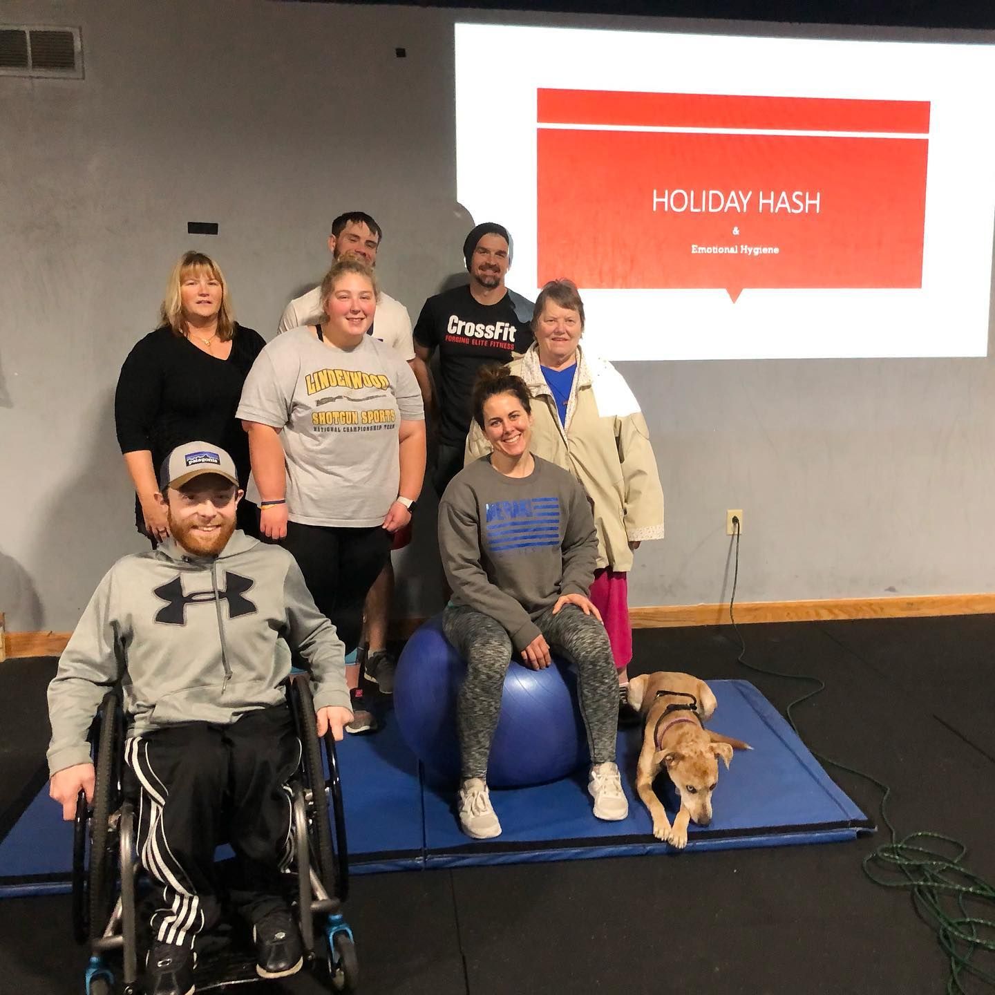Group photo of six people with a service dog on a blue mat in front of a presentation slide