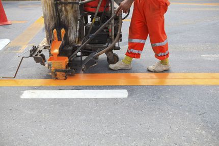 Road workers painting yellow lane markings with a road-striping machine on wet pavement.