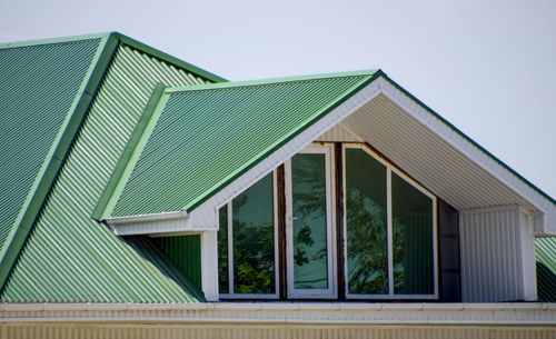 Green metal roof with dormer windows and white trim on a house exterior