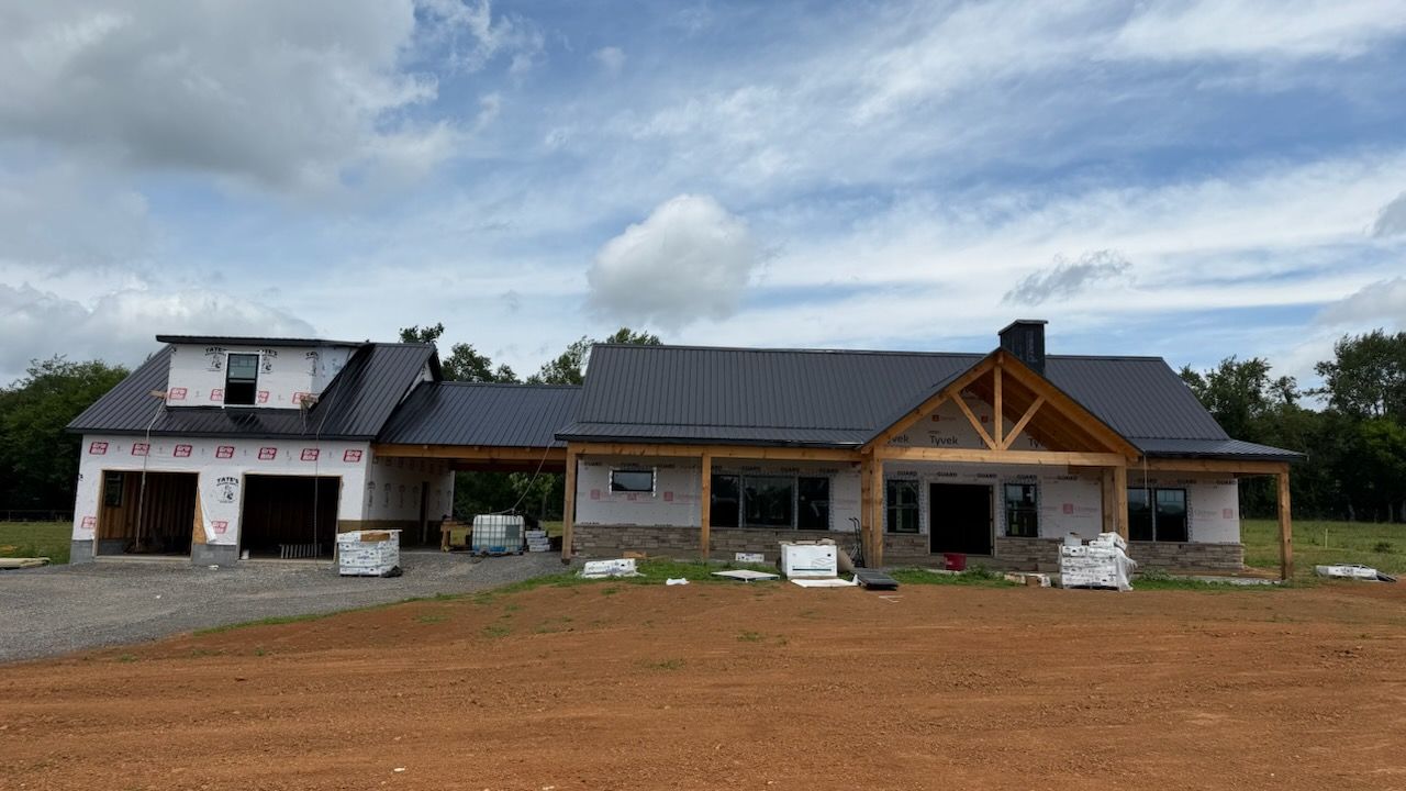 New house under construction with stone and wood exterior on a dirt lot under a cloudy sky
